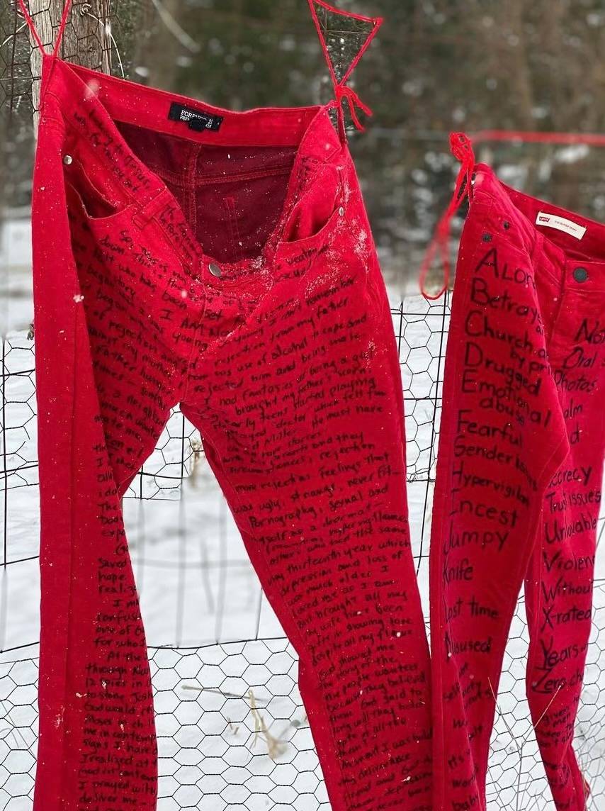 Pair of red jeans hanging on a fence, with a survivor's story inscribed on the jeans.